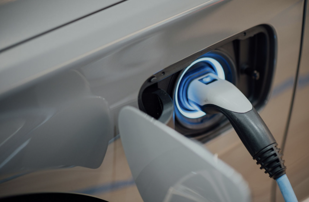 Close-up of an EV charging connector plugged into the vehicle’s port with a blue light ring.